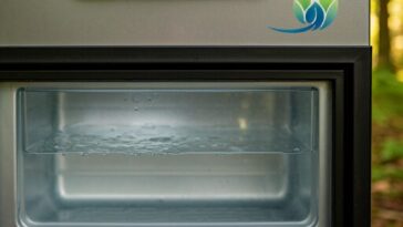 A close-up photo of a camping fridge door with water pooled at the bottom, reflecting the photographer.