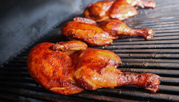 A beautifully presented smoked chicken half on a plate, showcasing its golden-brown skin and juicy meat, with herbs and sides in the background.