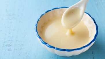 An opened can of evaporated milk with a spoon, set on a wooden kitchen countertop, highlighting its creamy texture and rich color.