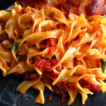 A bowl of egg noodles served with vegetables and sauce, showcasing their rich yellow color and texture, against a rustic background.