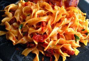 A bowl of egg noodles served with vegetables and sauce, showcasing their rich yellow color and texture, against a rustic background.