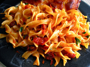 A bowl of egg noodles served with vegetables and sauce, showcasing their rich yellow color and texture, against a rustic background.