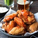 A vibrant plate of buffalo chicken wings drizzled with spicy buffalo sauce, served with a side of creamy blue cheese dressing, highlighting the perfect pairing of bold flavors in American cuisine.