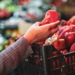 "A person inspecting fresh vegetables at a market, focusing on their vibrant colors and textures."