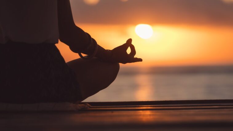 A serene scene depicting a person meditating in nature, surrounded by trees and soft sunlight. They sit cross-legged on a grassy area, eyes closed, embodying a sense of peace and tranquility. The image captures the essence of mindfulness and relaxation, emphasizing the importance of letting go of expectations during meditation.