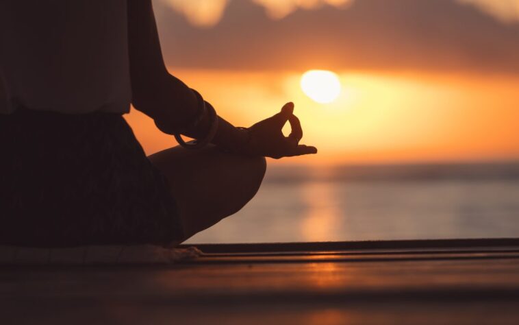 A serene scene depicting a person meditating in nature, surrounded by trees and soft sunlight. They sit cross-legged on a grassy area, eyes closed, embodying a sense of peace and tranquility. The image captures the essence of mindfulness and relaxation, emphasizing the importance of letting go of expectations during meditation.